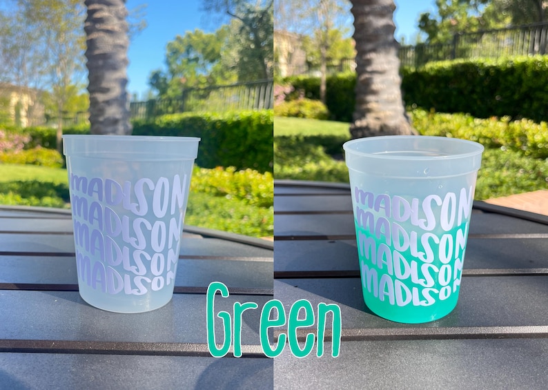 May include: A translucent plastic stadium cup featuring the name Madison repeated in white lettering. The cup on the left is clear, while the cup on the right shows a color-changing effect, transitioning to a vibrant green hue at the base.