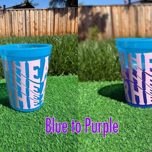 May include: A translucent plastic cup that changes color from blue to purple, featuring the word "RHEA" printed in a large, light pink, stylized font that repeats vertically down the side of the cup in a stacked, slightly offset design.