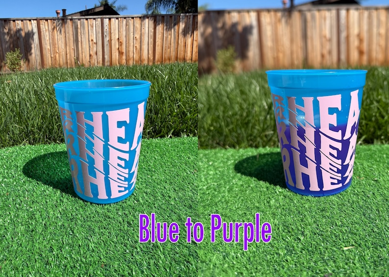 May include: A translucent plastic cup that changes color from blue to purple, featuring the word "RHEA" printed in a large, light pink, stylized font that repeats vertically down the side of the cup in a stacked, slightly offset design.