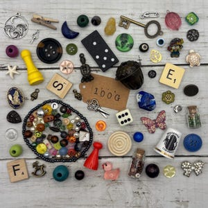May include: A collection of assorted craft supplies including buttons, beads, charms, game pieces, a domino, Scrabble tiles with letters S and E, a thimble labelled Mousehole Cornwall, a small glass bottle, and a tag with the text 100g.