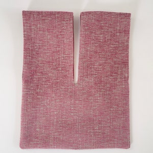 May include: A pink fabric bag with a V-shaped opening at the top. The fabric has a subtle textured pattern.