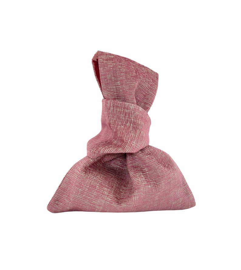 May include: A pink fabric gift bag with a knotted top. The bag is made of a textured material and has a slightly wrinkled appearance.
