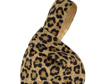 May include: A knot bag crafted from a tan fabric featuring a black and dark brown leopard print pattern. The bag has a single integrated handle loop that is formed by pulling one side of the fabric through the other, creating a knot.