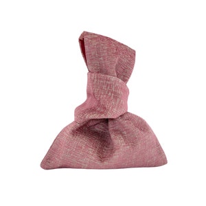 May include: A pink fabric gift bag with a knotted top. The bag is made of a textured material and has a slightly wrinkled appearance.