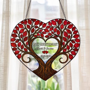 May include: Heart-shaped stained glass art piece with a tree design. The tree has red leaves and brown branches, with the text "40TH ANNIVERSARY David & Jessica 25.05.1986". Two red hearts are also included in the design. The piece is hanging from a chain.