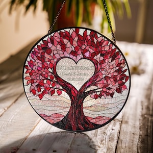 May include: A round stained glass window with a black metal frame. The design features a tree with a heart-shaped canopy and the text "40TH ANNIVERSARY David & Jessica 25.06.1985". The leaves are red and pink.