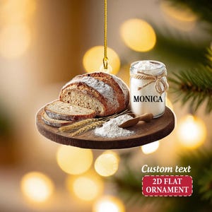 May include: A 2D flat ornament featuring a loaf of sliced bread, a jar of flour with "MONICA" printed on it, and a wooden spoon. The ornament also includes the text "Custom text" and "2D FLAT ORNAMENT".