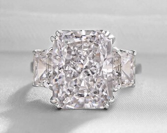 May include: A three-stone engagement ring with a large, rectangular-cut center stone and two smaller, square-cut side stones. The ring is set in a silver band and sparkles brightly.