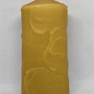Peut inclure: Une bougie en cire d'abeille cylindrique et haute, avec une surface texturée naturelle. La bougie est de couleur jaune foncé et a une petite mèche en haut.