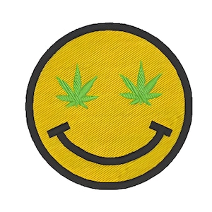 May include: Yellow smiley face with green marijuana leaf eyes. The smiley face is outlined in black and has a black smile.