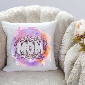 May include: White throw pillow with a watercolor design of flowers and the word "MOM" in a circle. The pillow is on a white armchair with a floral pattern.