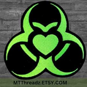 May include: A green biohazard symbol with a heart in the center. The symbol is outlined in black and the heart is filled in with green. The background is a dark gray brick wall.