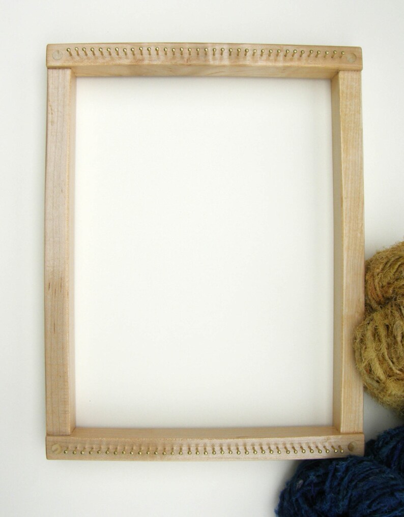 Puede incluir: Un telar de madera con tachuelas de lat&oacute;n alrededor del per&iacute;metro. El telar est&aacute; vac&iacute;o y listo para tejer. Dos ovillos de hilo est&aacute;n en la esquina inferior derecha de la imagen.
