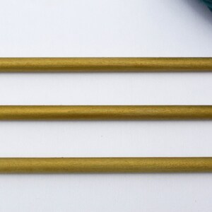 May include: Three gold-colored wooden knitting needles on a white background.