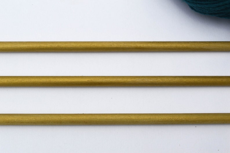 May include: Three gold-colored wooden knitting needles on a white background.