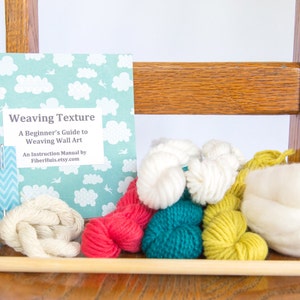 May include: A weaving kit with a book titled "Weaving Texture", yarn in various colors, needles, and a wooden dowel. The book has a light blue cover with white clouds. Yarn colors include white, red, teal, and yellow.