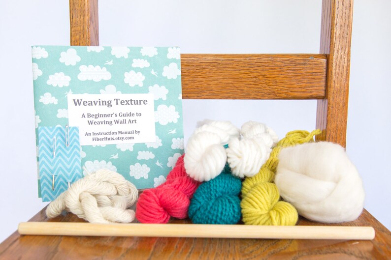 May include: A weaving kit with a book titled "Weaving Texture", yarn in various colors, needles, and a wooden dowel. The book has a light blue cover with white clouds. Yarn colors include white, red, teal, and yellow.