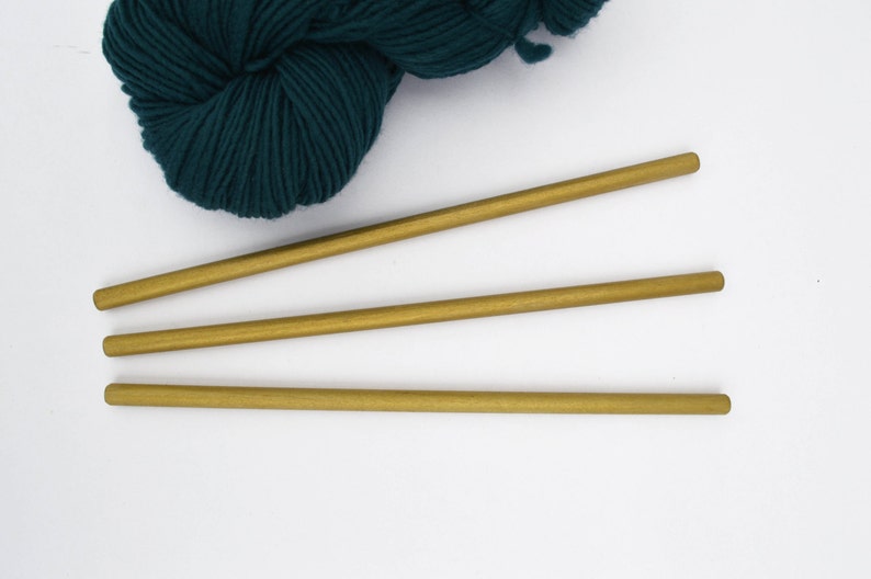 May include: Three gold knitting needles on a white background with a ball of teal yarn.