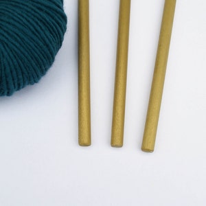 May include: Three gold knitting needles with a ball of teal yarn.