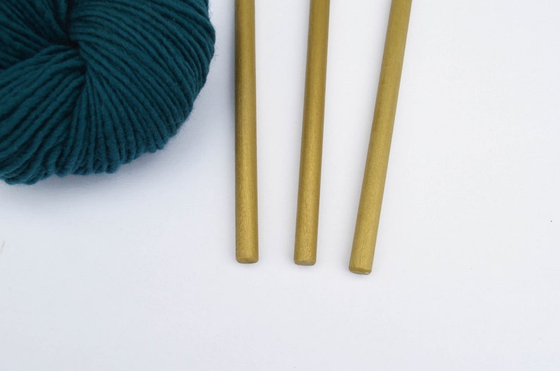 May include: Three gold knitting needles with a ball of teal yarn.