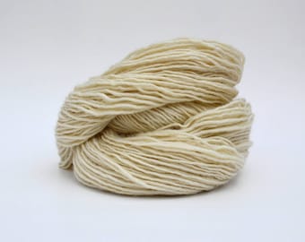 Puede incluir: Un ovillo de hilo de color blanco roto, hecho de fibras naturales, está enrollado de forma suelta y listo para tejer o hacer ganchillo.