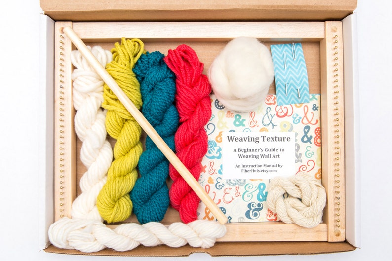 May include: A weaving kit in a cardboard box, featuring a wooden frame, various colored yarns (white, yellow-green, teal, red), a wooden dowel, and a book titled "Weaving Texture". The book is a beginner's guide to weaving wall art.