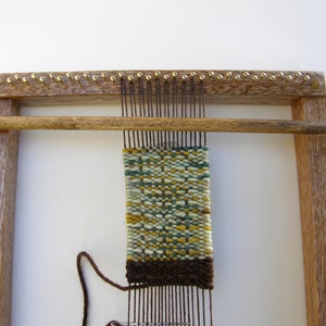May include: A wooden loom with a brown, green, and yellow woven tapestry on it. The loom has a wooden frame and a wooden bar that is used to move the warp threads.