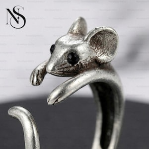 Op de afbeelding: Een zilverkleurige ring met een gedetailleerd muisontwerp. De muis heeft zwarte edelsteenogen en is gebeeldhouwd met getextureerde vacht en grote oren. De band van de ring vormt de staart van de muis.