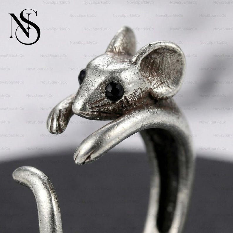 Op de afbeelding: Een zilverkleurige ring met een gedetailleerd muisontwerp. De muis heeft zwarte edelsteenogen en is gebeeldhouwd met getextureerde vacht en grote oren. De band van de ring vormt de staart van de muis.