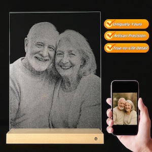 Könnte beinhalten: Ein personalisiertes Foto, das auf einer transparenten Glasplatte geätzt und auf einem Holzsockel montiert ist. Das Bild zeigt ein lächelndes älteres Ehepaar. Auf der rechten Seite stehen die Worte "Uniquely Yours", "Artisan Precision" und "True-to-Life Detail".