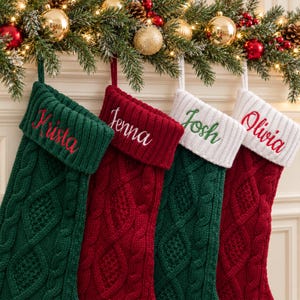 Könnte beinhalten: Vier Weihnachtsstrümpfe aus Zopfstrick mit umgeschlagenen Bündchen. Der erste ist grün mit roter Stickerei Krista, der zweite rot mit weißer Stickerei Jenna, der dritte grün mit grüner Stickerei Josh und der vierte rot mit roter Stickerei Olivia.