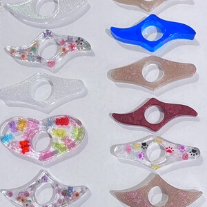 May include: Assortment of colorful book marks with various designs, including glitter, flowers, and paw prints. The book marks are made of clear plastic and have a ring to hold the page.