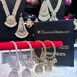 Op de afbeelding: Een assortiment diamanten sieraden, waaronder kettingen, oorbellen en armbanden. De kettingen en oorbellen worden op zwarte standaards getoond, de armbanden op een rode fluwelen staaf. De sieraden zijn sprankelend en sierlijk.