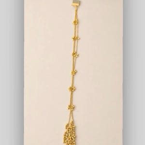 May include: A gold-colored hair accessory featuring a series of delicate floral accents and a cascade of small, round beads. The accessory is designed to be worn in the hair, adding a touch of elegance. The design includes multiple strands and a secure attachment.