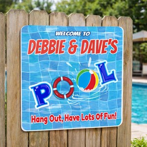 personalized pool sign mounted on wooden fence near backyard swimming pool with beach ball and lifebuoy graphics