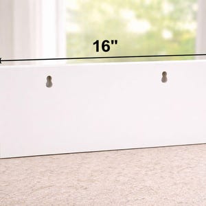 May include: A white rectangular wooden shelf, 40.6 cm long and 12.7 cm high, with two keyhole slots for hanging. The shelf is displayed on a light-colored surface, with a plant in a white pot visible in the background.