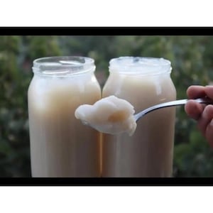 May include: Two clear glass jars filled with a white, creamy substance. A spoon holds a scoop of the substance.