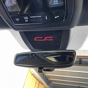 Op de afbeelding: Een zwart auto-interieur met een achteruitkijkspiegel en een zwart paneel met de tekst "PASSENGER AIR BAG" en "C 45" in rode letters.