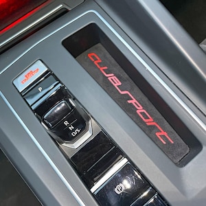 Può includere: Primo piano del cambio di marcia di un'auto con la scritta "CLUBSPORT" sulla console. Il cambio ha pulsanti per "P", "R", "N" e "D/S".