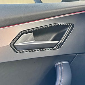 Può includere: Primo piano dell'interno di una portiera di un'auto con una finitura in fibra di carbonio per la maniglia della portiera. La maniglia è argentata e ha un contorno in fibra di carbonio nero.