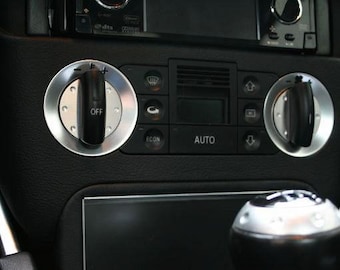 May include: Close-up of a car's dashboard featuring climate control knobs and buttons. The knobs are silver with black centers, one labeled "OFF." Buttons include "AUTO" and icons for various functions. The gear shift is visible in the foreground.