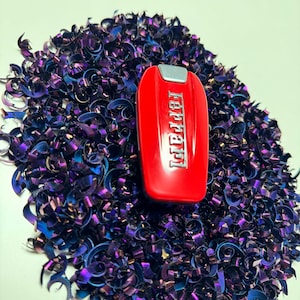 May include: A red key fob with the word "Ferrari" in silver lettering, surrounded by a pile of iridescent purple and blue metal shavings.