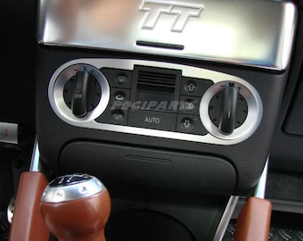 May include: Close-up of a car's interior, featuring a black dashboard with silver accents. The image highlights the climate control panel with dials and buttons, and a gear shift knob. The text "POGIPARTS" and "AUTO" are visible.