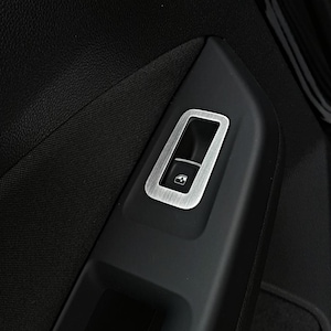 Könnte beinhalten: Nahaufnahme eines schwarzen Autotürpanels mit einem silbernen Fenstersteuerungsschalter. Der Schalter hat eine gebürstete Metalloberfläche und ein kleines Fenstersymbol.