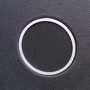 Puede incluir: Una rejilla de altavoz circular con un borde plateado. La rejilla tiene un patrón negro en forma de panal. El fondo es una superficie texturizada de color gris oscuro.