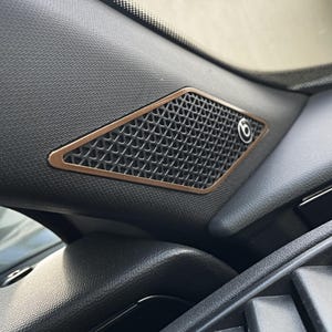 May include: A black speaker grille with a copper-colored trim and a Beats logo. The speaker is mounted in a car's interior.