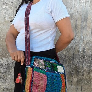 Pode incluir: Uma bolsa tiracolo quadrada com um design de patchwork de v&aacute;rios quadrados de tecido coloridos em tons de azul, rosa, amarelo e verde, acentuada com bordados de ponto corrido vis&iacute;veis e uma al&ccedil;a de ombro tecida e estampada.