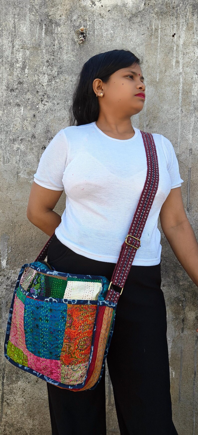 Pode incluir: Uma bolsa tiracolo com design de patchwork apresentando v&aacute;rios quadrados de tecido coloridos em tons de azul, rosa, laranja e branco, acentuada por bordados vis&iacute;veis de ponto corrido e uma al&ccedil;a longa ajust&aacute;vel com um padr&atilde;o vermelho escuro e azul.