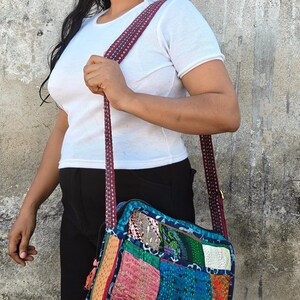 Pode incluir: Uma bolsa tiracolo de formato quadrado com um design de patchwork feito de v&aacute;rios retalhos de tecido coloridos em tons de azul, rosa, verde e laranja, acentuada com costuras kantha intrincadas e uma al&ccedil;a de ombro longa com padr&atilde;o vermelho escuro.