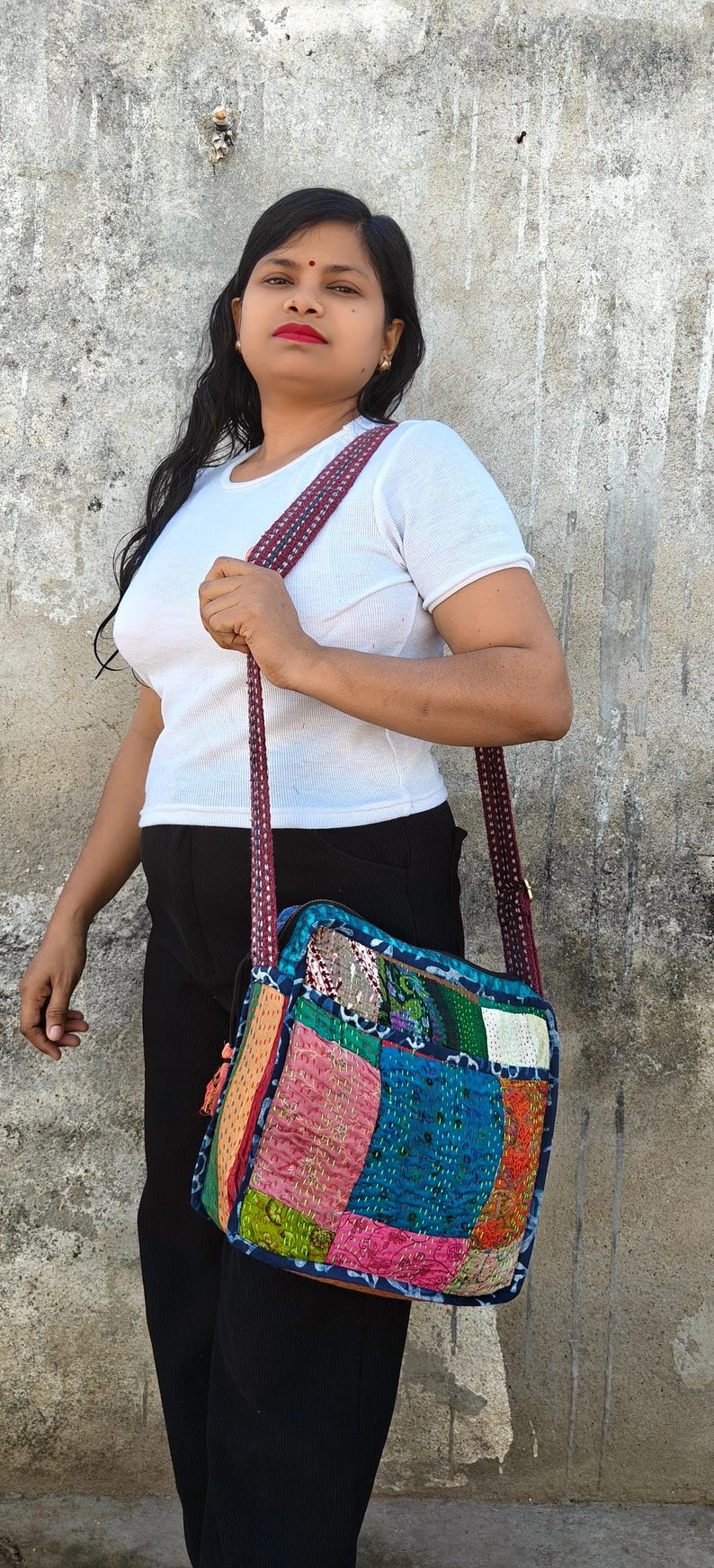 Pode incluir: Uma bolsa tiracolo de formato quadrado com um design de patchwork feito de v&aacute;rios retalhos de tecido coloridos em tons de azul, rosa, verde e laranja, acentuada com costuras kantha intrincadas e uma al&ccedil;a de ombro longa com padr&atilde;o vermelho escuro.